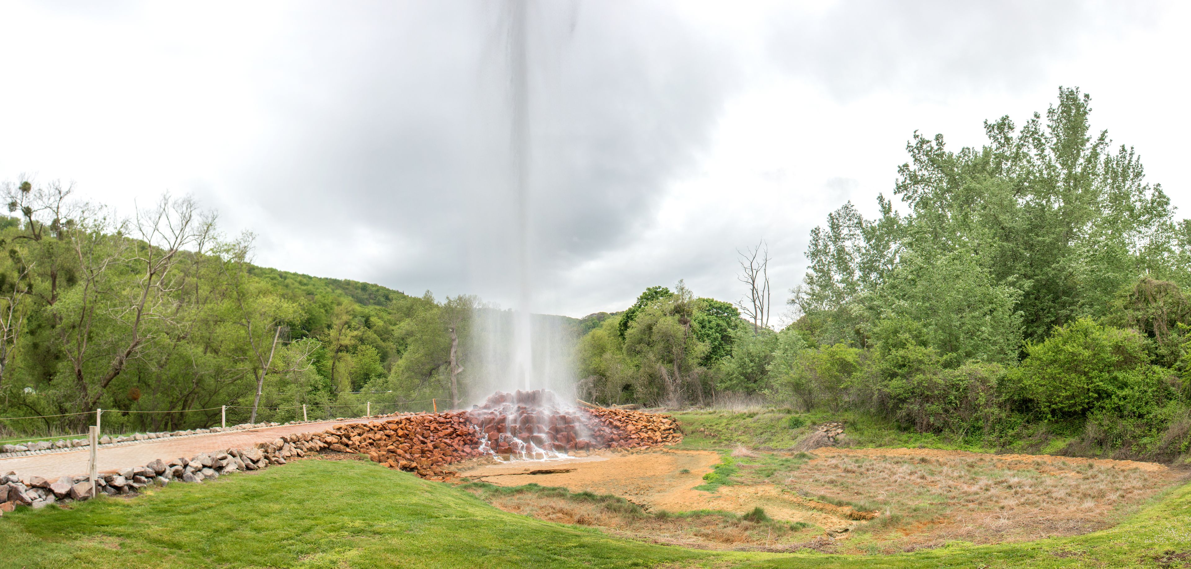 Une cascade d’eau se déversant sur un promontoire rocheux, entourée d’une végétation luxuriante et d’arbres.