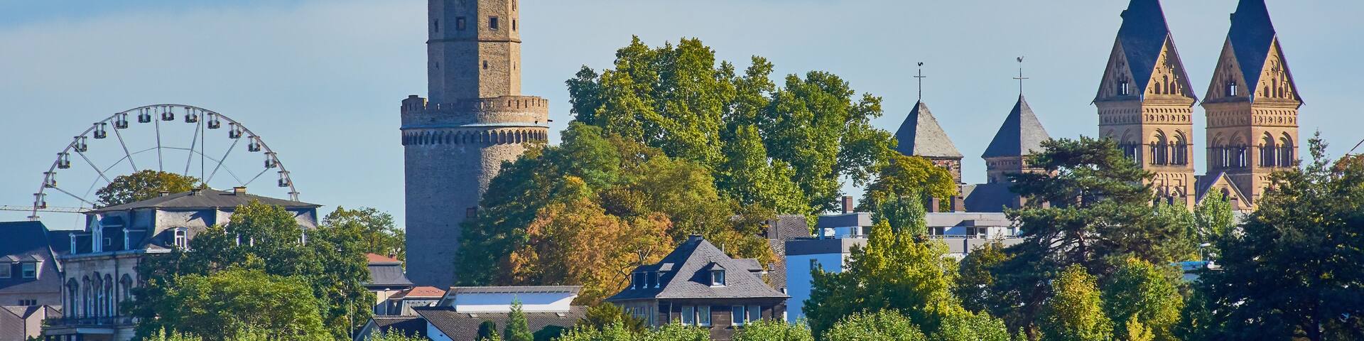 A historic tower with a clock, a church with pointed spires, and a Ferris wheel.