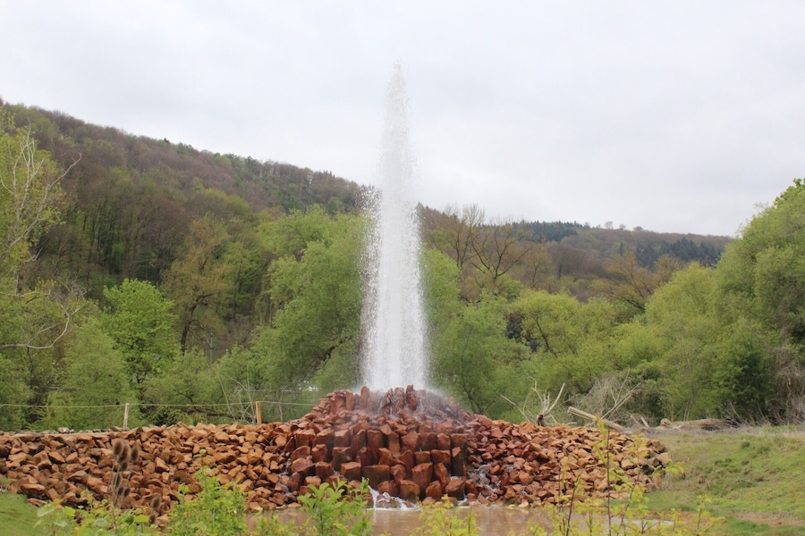 Una fuente de piedra en un área boscosa, con un montículo de rocas en primer plano.