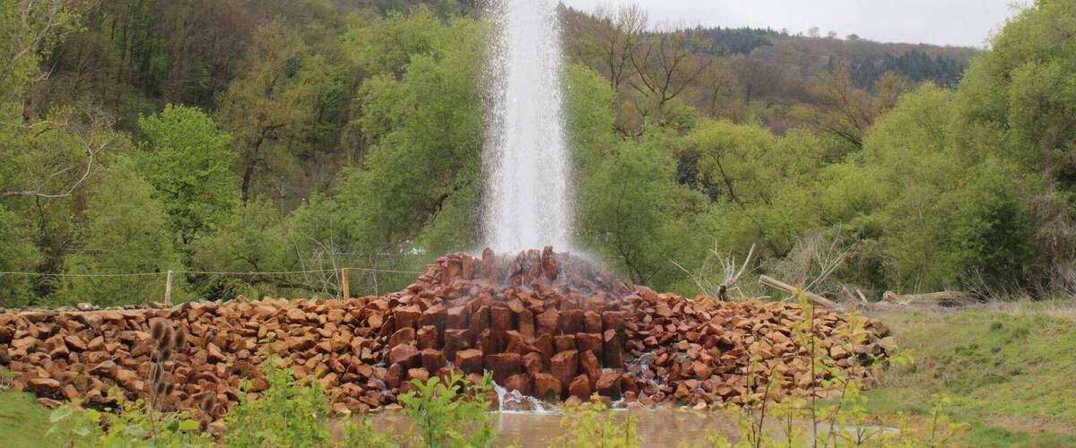 A rock fountain in a forested area with a pile of rocks in the foreground.