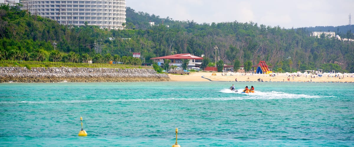 A beach with a large hotel, a lifeguard tower, and a water sports area.