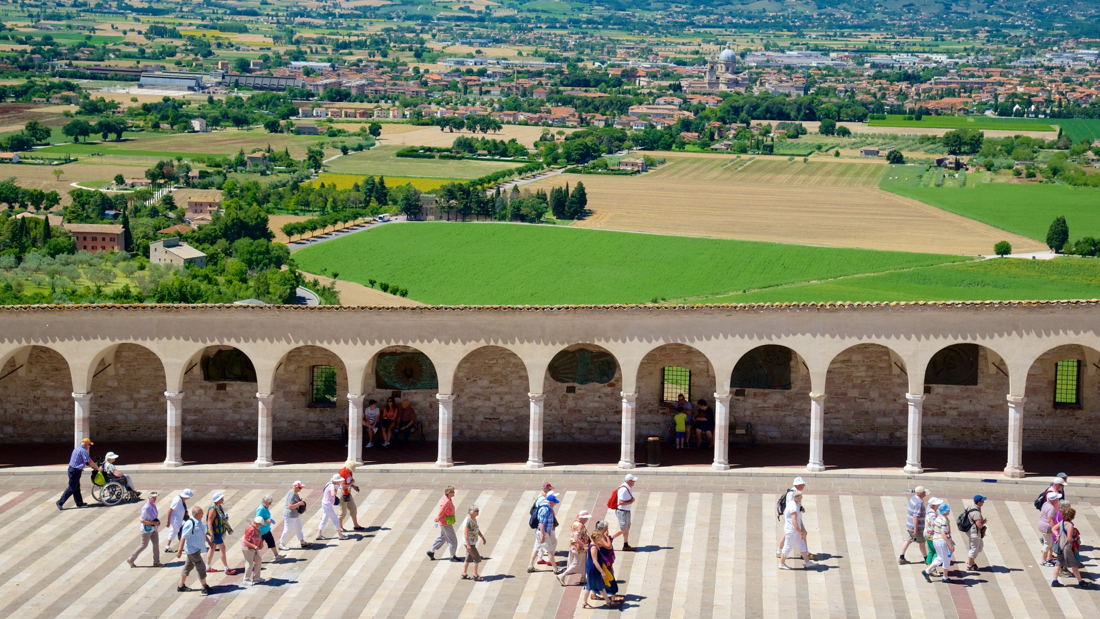 A historical square with a row of arches and people walking.