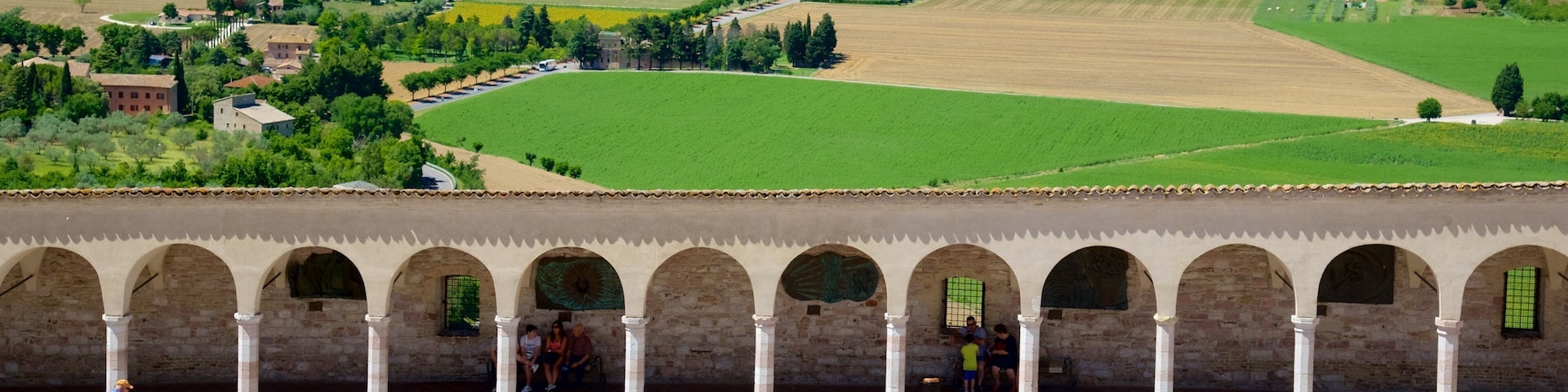 A historical square with a row of arches and people walking.