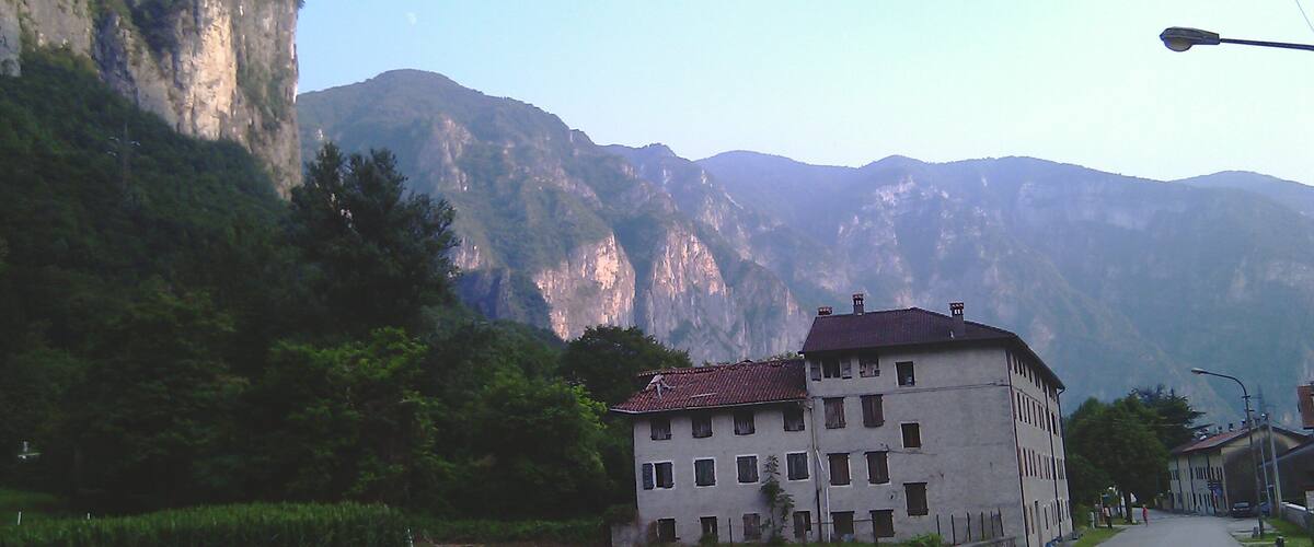 A building with a red-tiled roof, surrounded by lush greenery and mountains in the background.