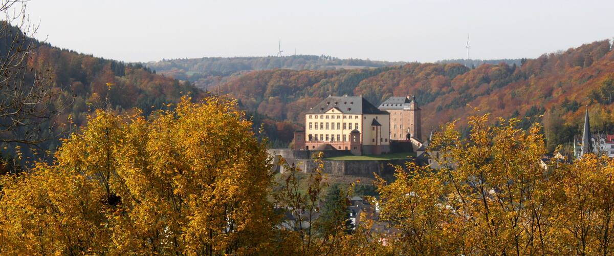 A castle surrounded by autumn-colored trees and hills.