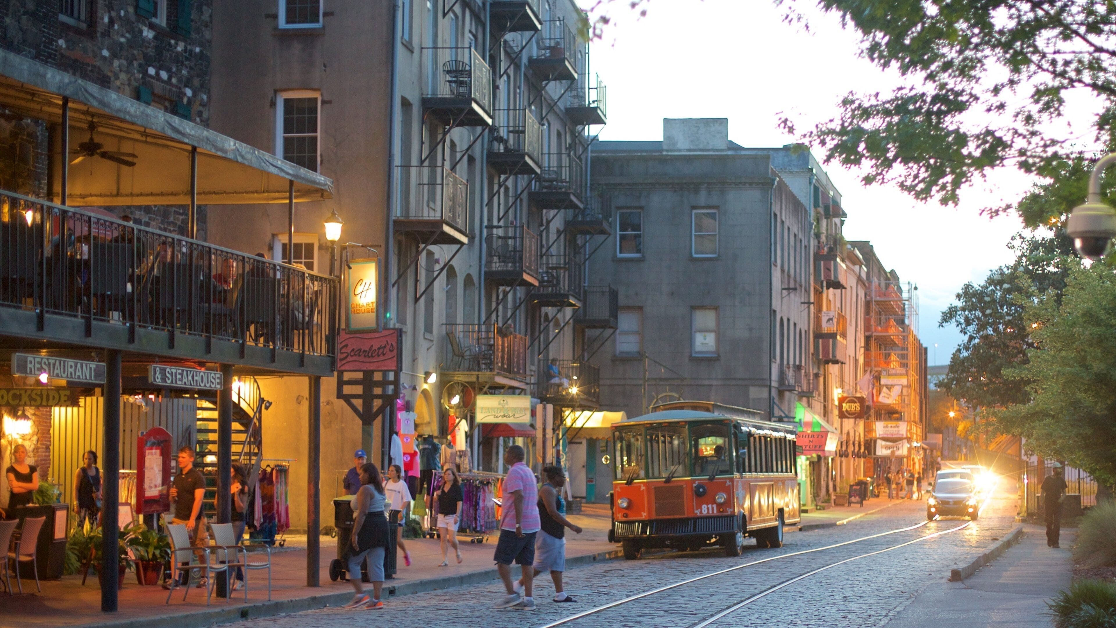 Una calle adoquinada con un tranvía, tiendas y peatones.