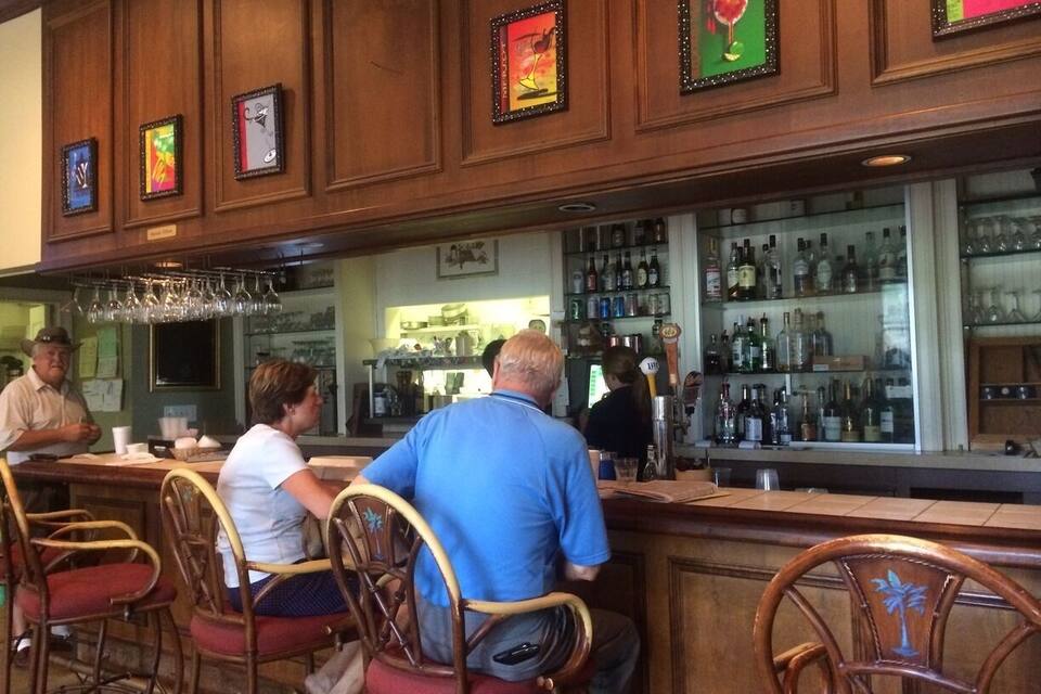 A bar with wooden paneling, framed artwork, and patrons seated at tables.