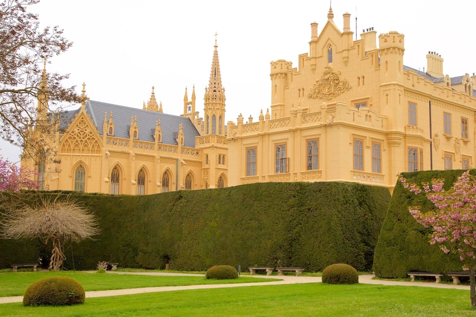 A grand castle with a large garden, a tall spire, and a well-manicured lawn.