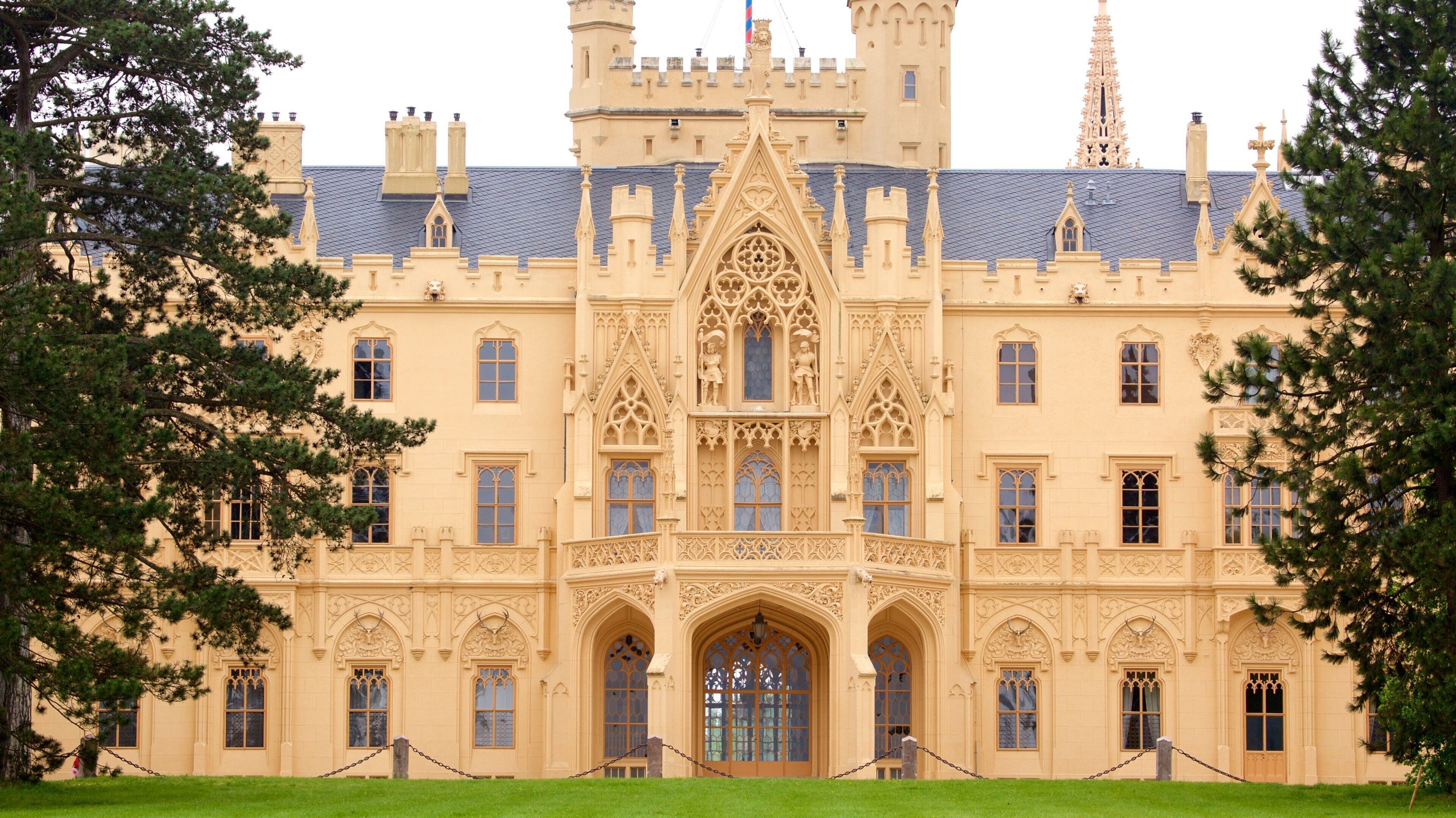 A large, ornate castle with a central tower, arched windows, and a well-maintained lawn.