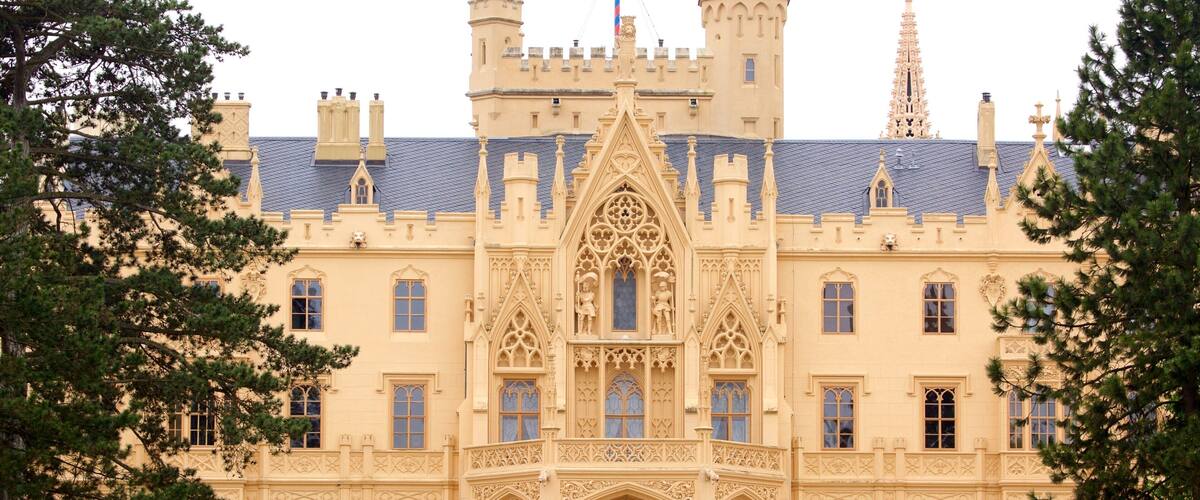 A large, ornate castle with a central tower, arched windows, and a well-maintained lawn.