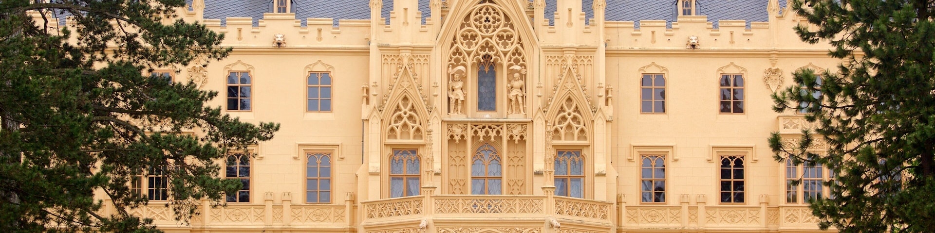 A large, ornate castle with a central tower, arched windows, and a well-maintained lawn.