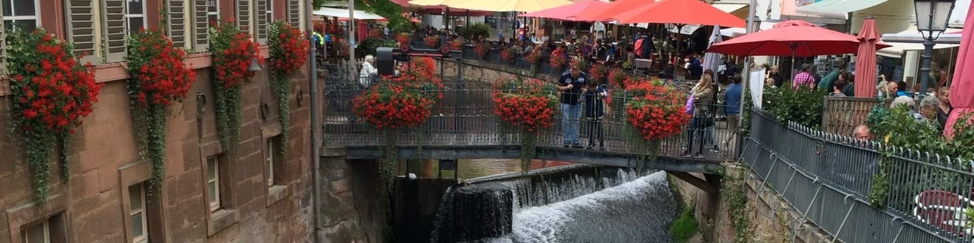 A small waterfall in a town square with buildings on either side.