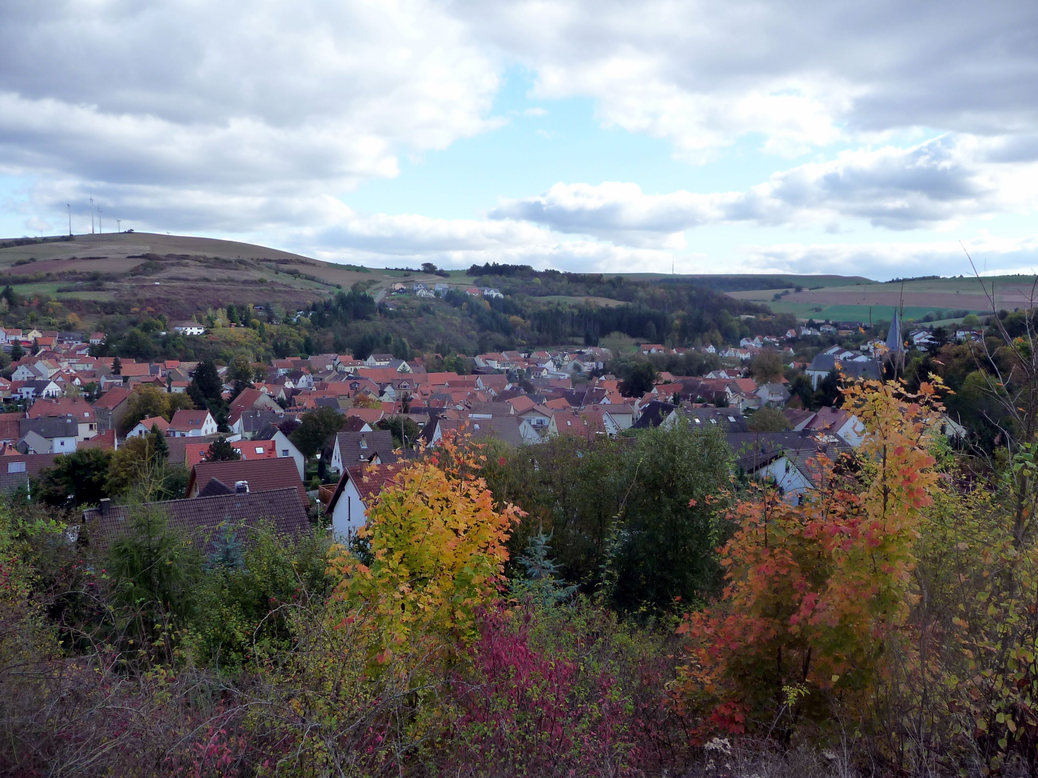 A town with red-roofed houses, autumn foliage, and a church steeple.