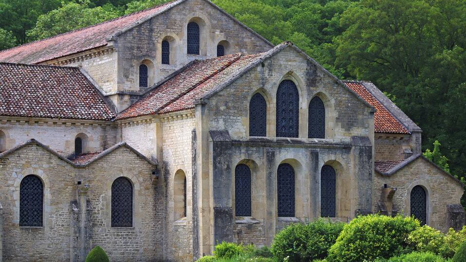 A historic stone church with arched windows and a tiled roof, surrounded by lush greenery.