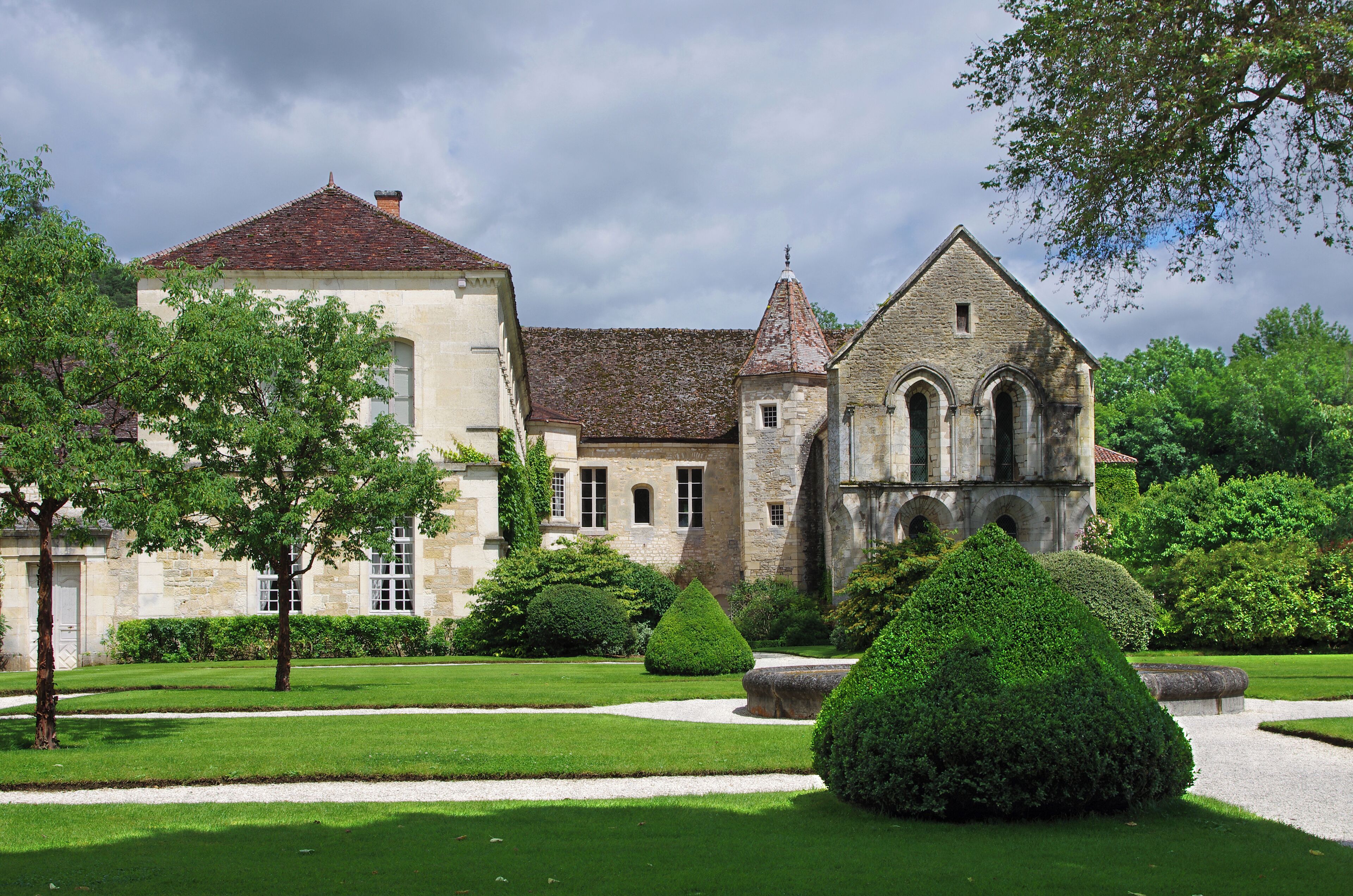 A historic building with a red-tiled roof, surrounded by well-manicured gardens and hedges.