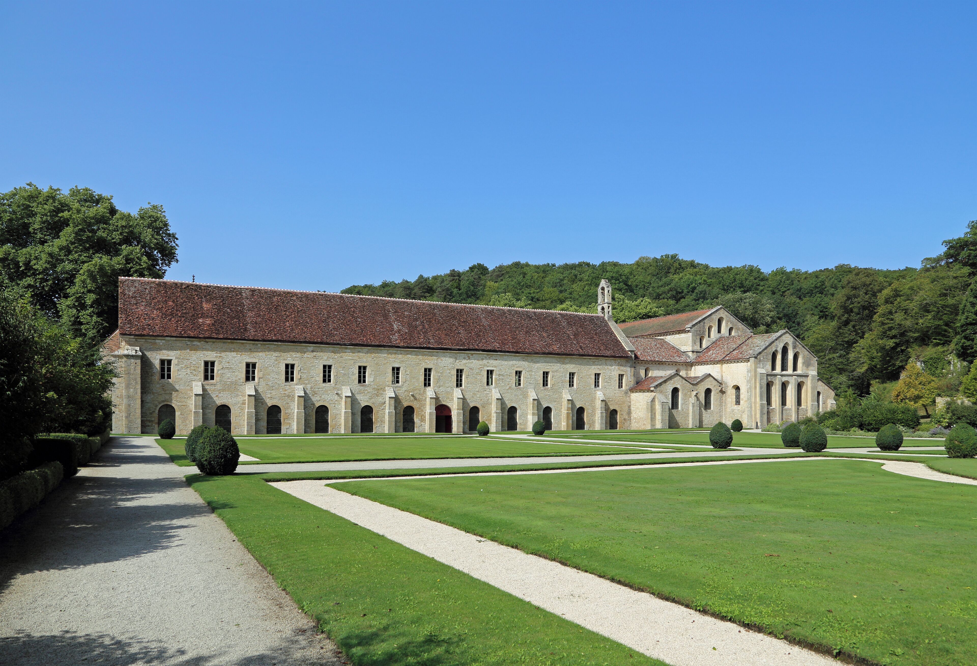 A large, historic building with a long facade and arched windows, surrounded by well-manicured lawns and a clear blue sky.
