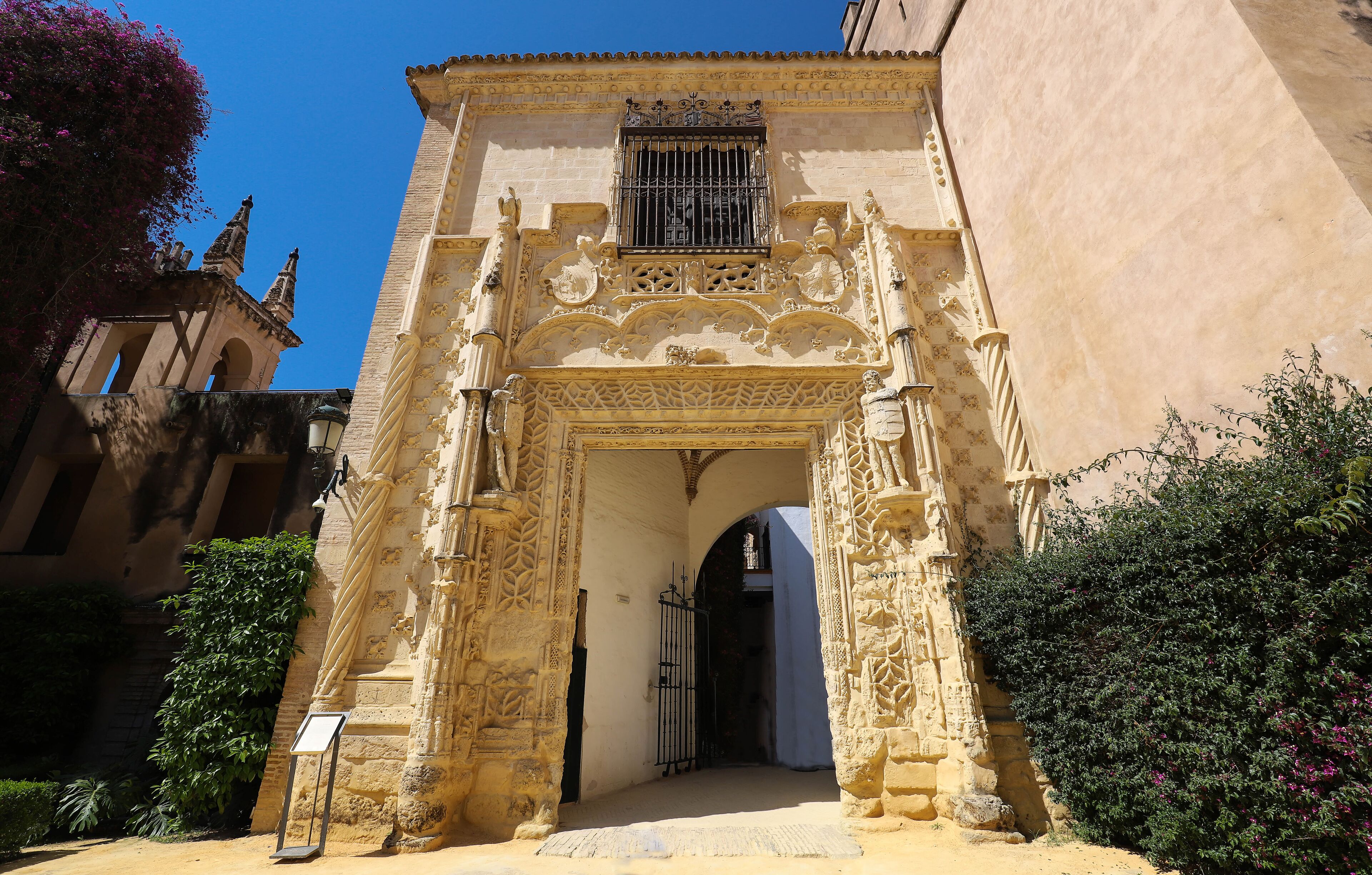An ornate stone archway with intricate carvings and a barred window, leading into a building.