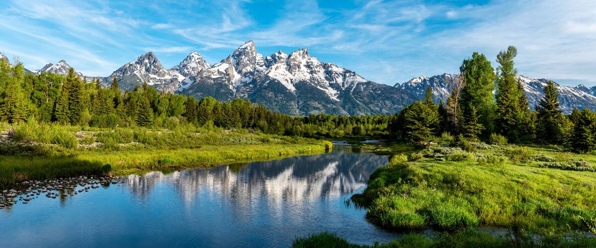 A mountain range with a clear lake reflecting the peaks, surrounded by lush greenery.