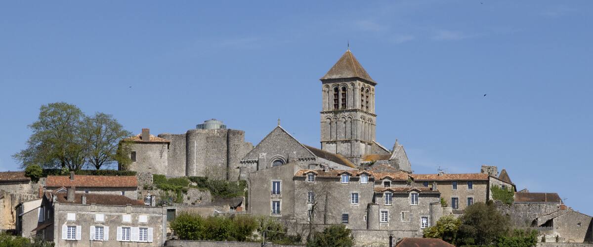 A historic stone building with a bell tower and a large tree in the foreground.