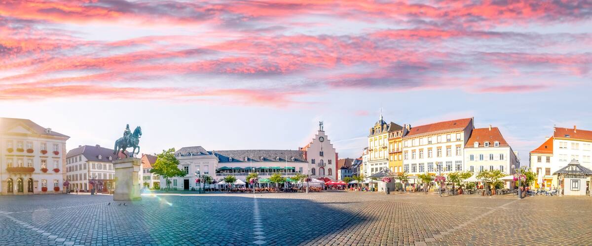 A cobblestone square with historic buildings, a statue, and a church.