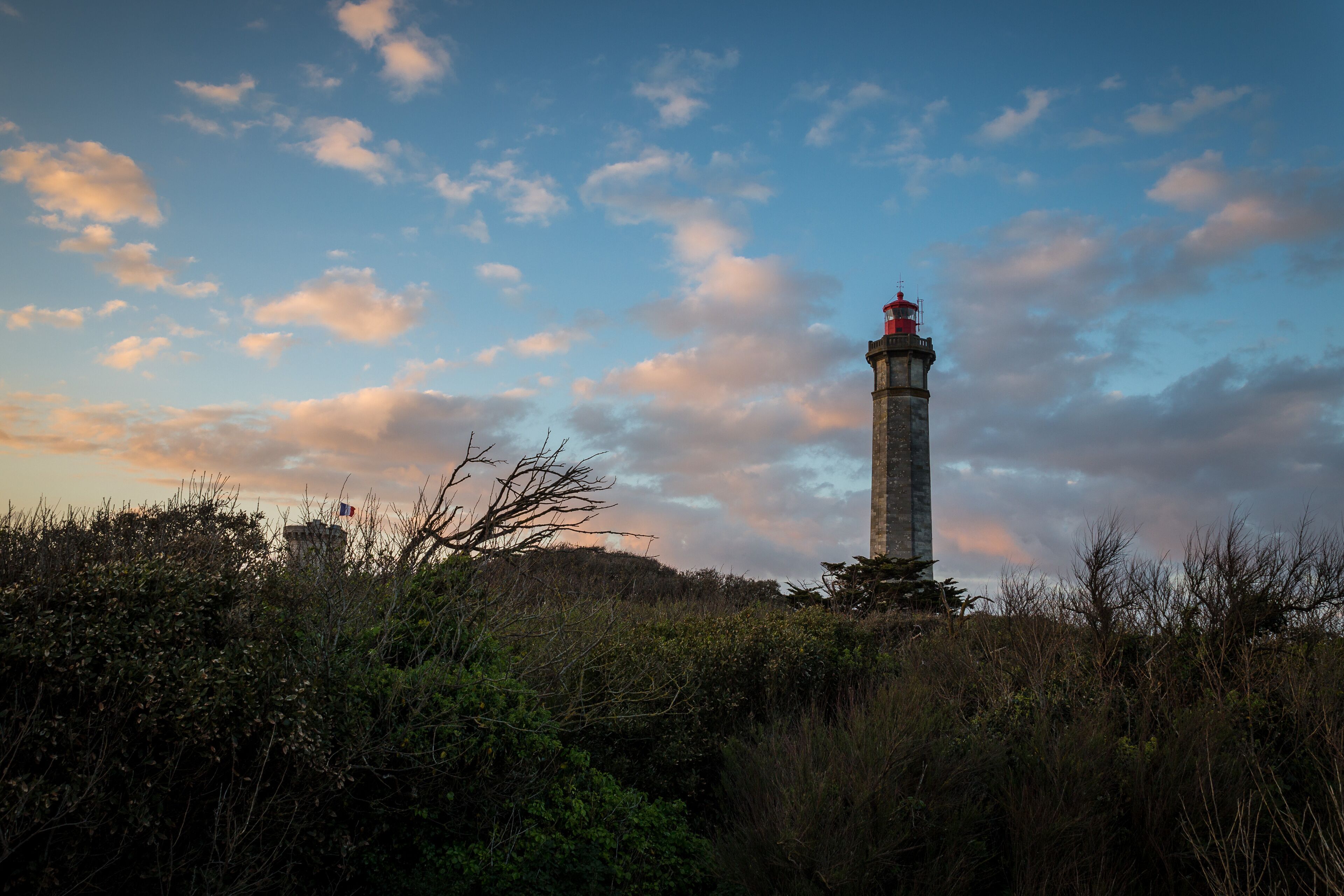 A lighthouse on a hill with a clear sky and scattered clouds.