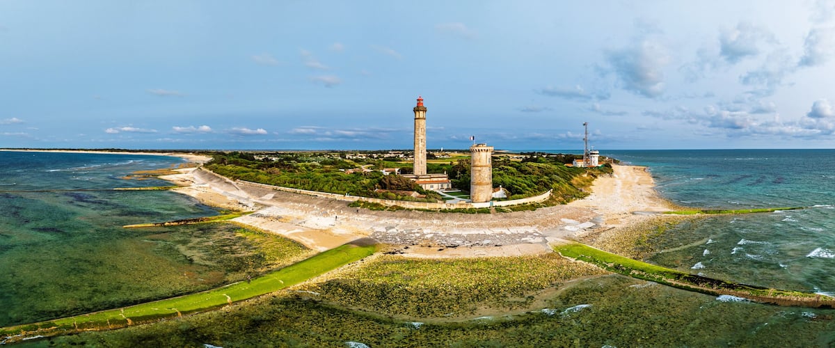 An aerial view of a coastal lighthouse surrounded by clear waters and greenery.