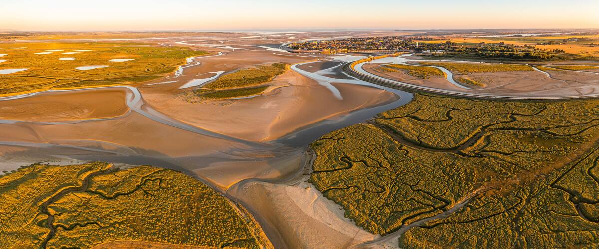 An aerial view of a coastal landscape with winding rivers, sand dunes, and a small town with buildings.