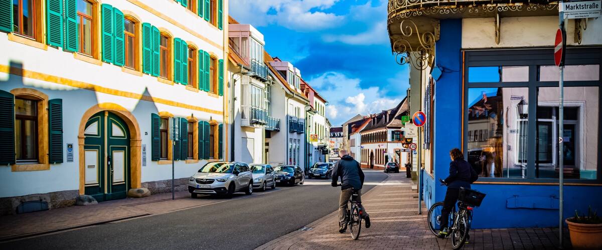 A street with buildings, a cyclist, and parked cars.
