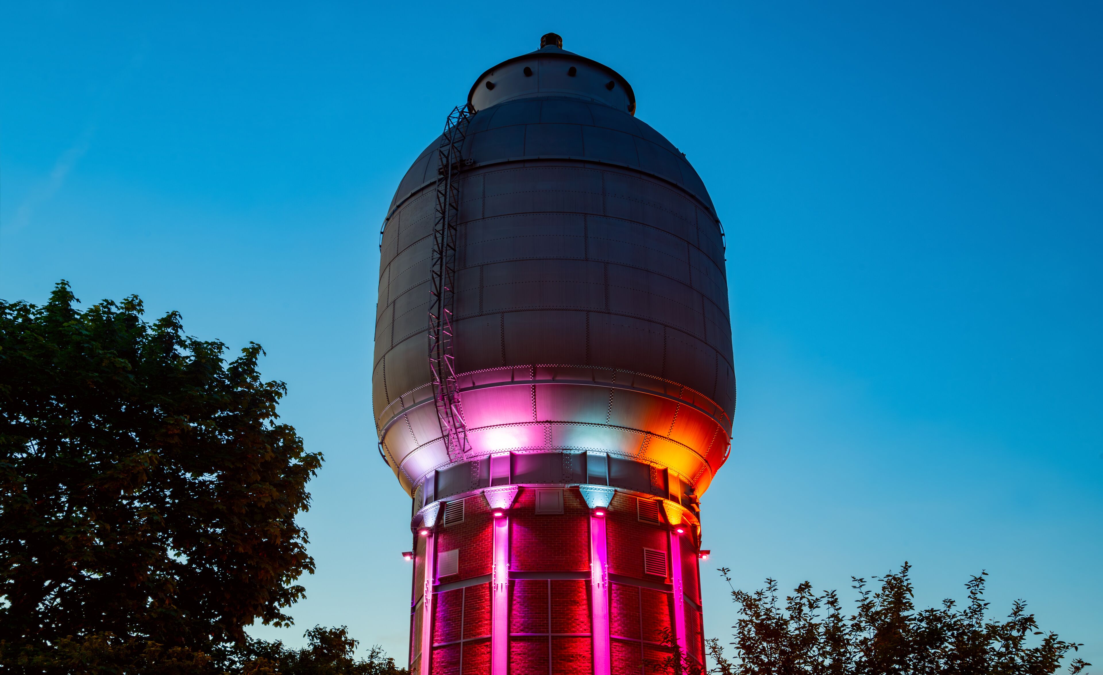 A water tower with a dome and a cylindrical base, illuminated with pink and red lights.