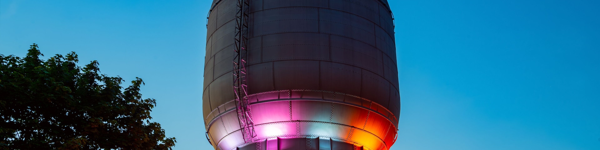 A water tower with a dome and a cylindrical base, illuminated with pink and red lights.