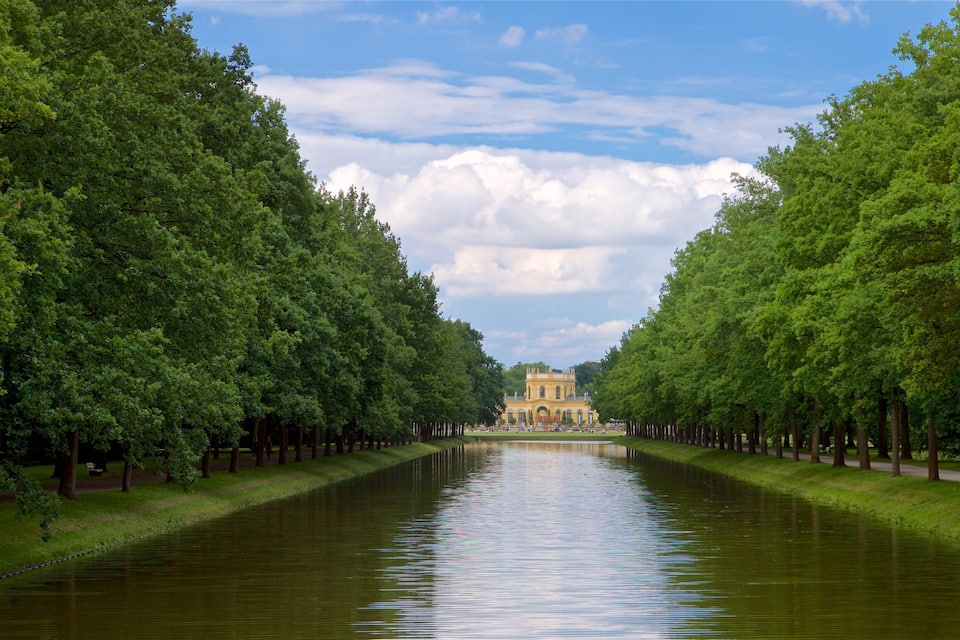 A canal flanked by trees leading to a classical building.