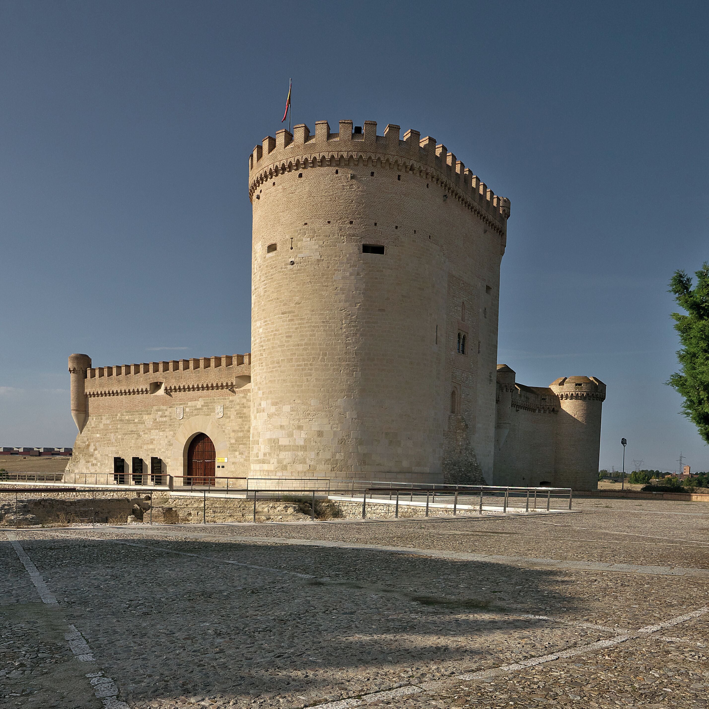 A historic stone tower with a round tower and a rectangular entrance, surrounded by a gravel area.