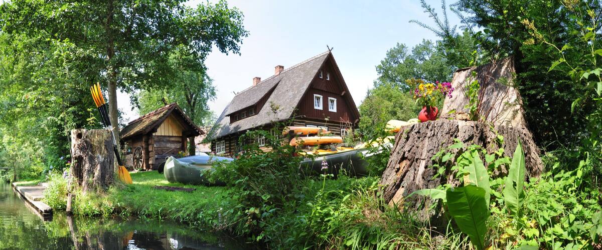 A wooden house by a river with a boat and a tree stump.