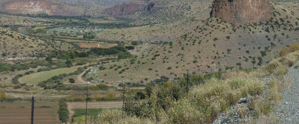 A rugged landscape with a prominent rock formation, a winding road, and sparse vegetation.
