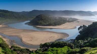 Paisagem costeira com rio, praias de areia e colinas verdejantes.