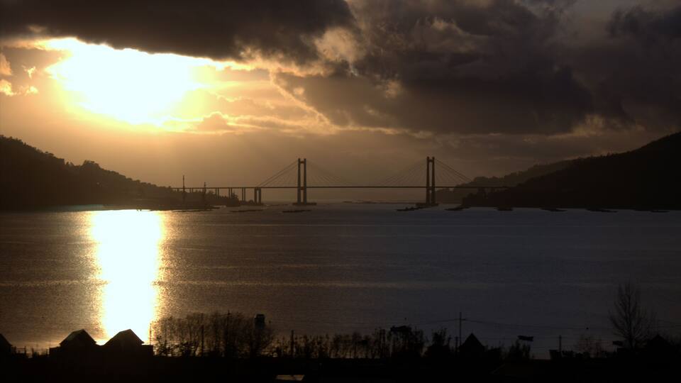 A sunset over a bridge with a body of water in the foreground.