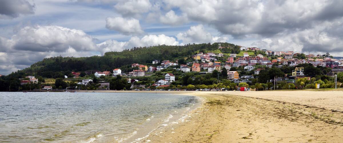 A beach with clear water, a sandy shore, and a hillside with colorful houses in the background.