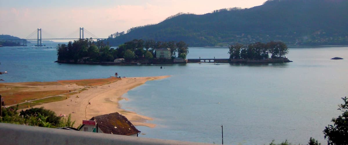 A coastal landscape with a beach, a bridge, and a forested hill.