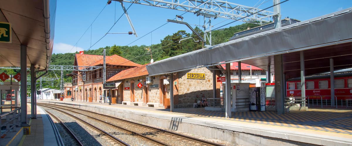 A train station with two platforms, a stone building, and overhead electrical lines.