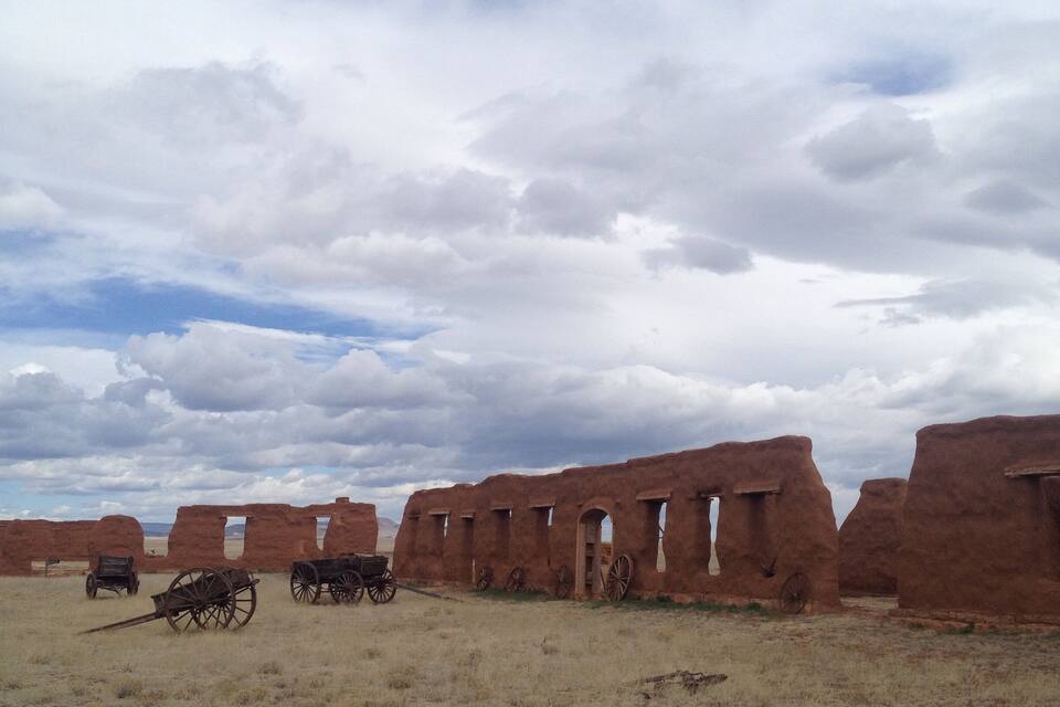 A historical site with adobe ruins and old wooden wagons.