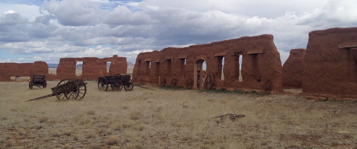 A historical site with adobe ruins and old wooden wagons.