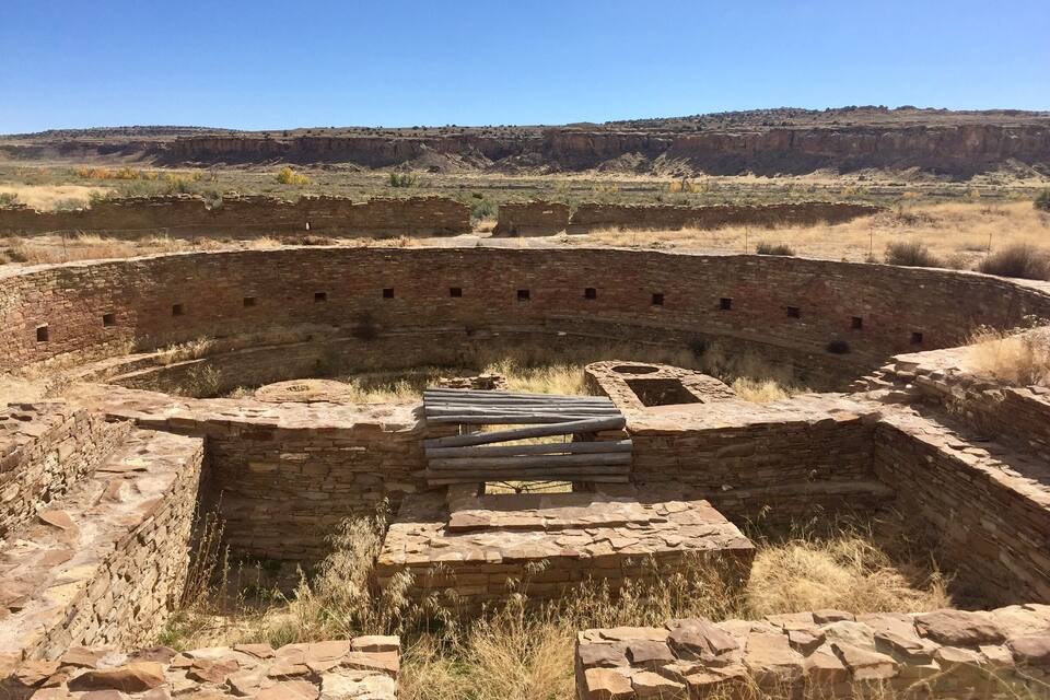 Un'antica struttura in pietra con un cortile centrale circondato da mura, immersa in un paesaggio collinare e arido.