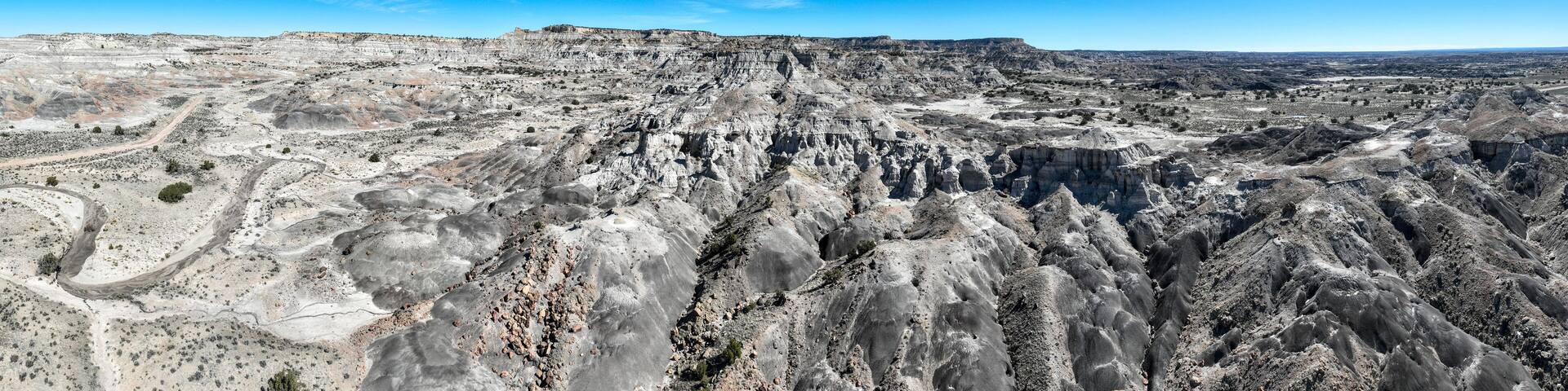 A vast, rugged landscape with layered rock formations and a clear blue sky.