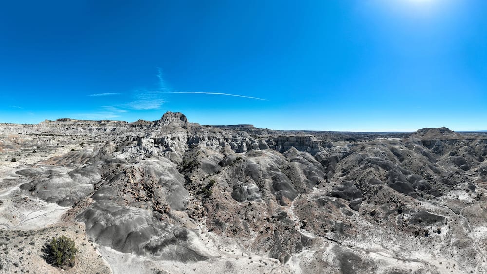 Eine zerklüftete Schluchtlandschaft mit einem markanten Felsspitze und geschichteten Gesteinsschichten unter blauem Himmel.