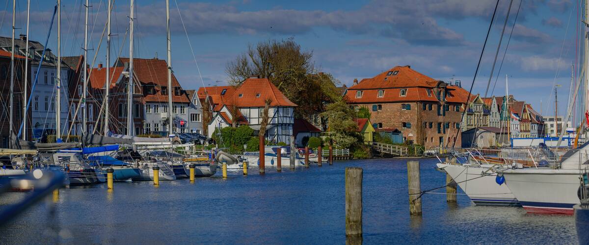 A marina with boats docked, surrounded by traditional European houses with red roofs.