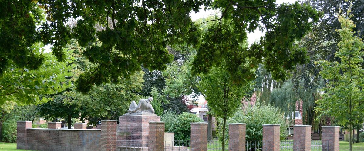A cemetery with brick walls and a statue, surrounded by trees and grass.