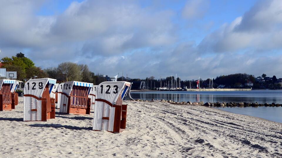 Beach chairs numbered 123, 124, and 129 on a sandy beach with a calm body of water and a cloudy sky in the background.