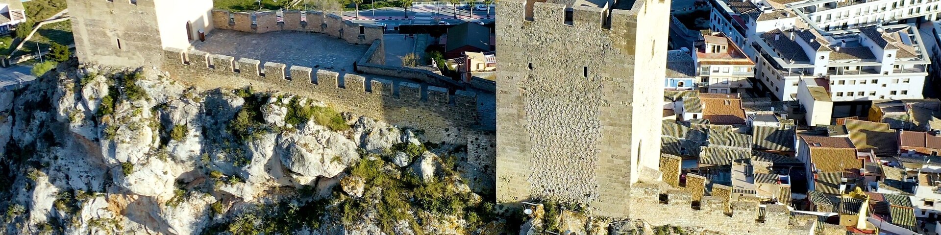 Un castillo de piedra en la cima de una colina rocosa, con un pueblo abajo.
