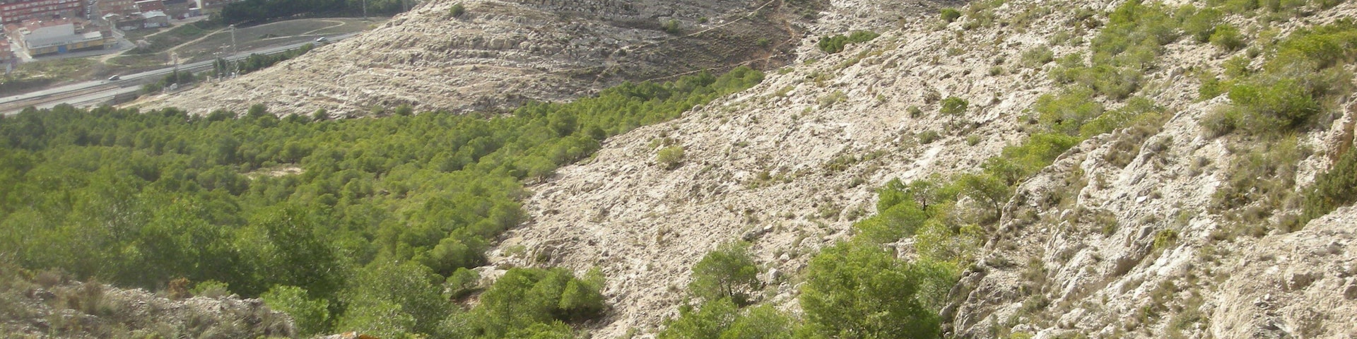 Rambla del Conejo, en la Sierra de la Villa (sendero PR-CV 312). En primer plano la rambla, detrás la mitad norte de Villena y el polígono industrial El Rubial, más allá El Polovar y los Cabezos y al fondo la sierra Alhácera (o Lácera) y el altiplano murciano.