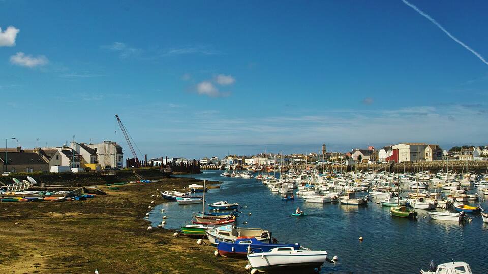 A harbor filled with boats, a sandy beach, and buildings along the shore.